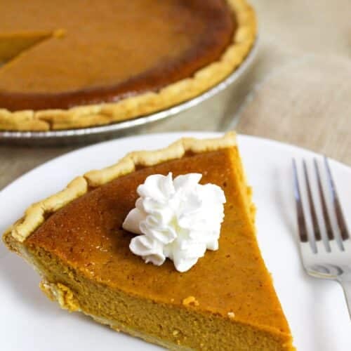 pumpkin pie on a white plate with whipped cream.