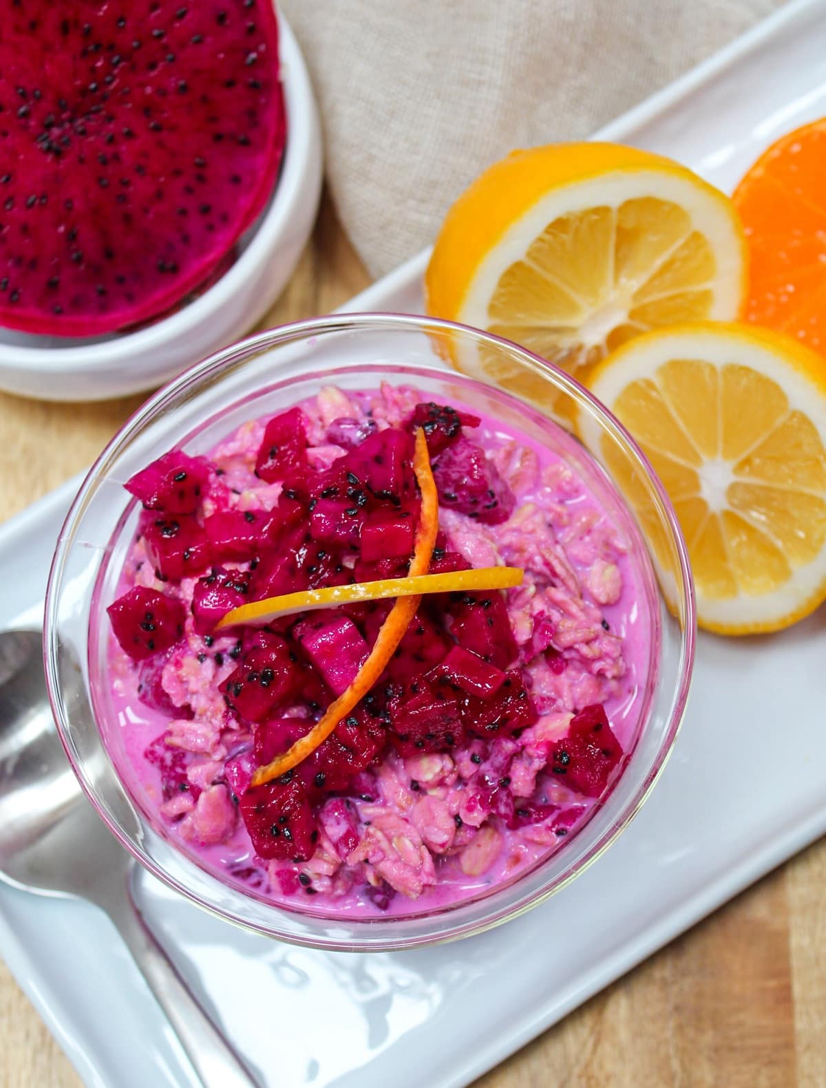 Pink overnight oats topped with chopped dragon fruit and citrus zest in a glass bowl.