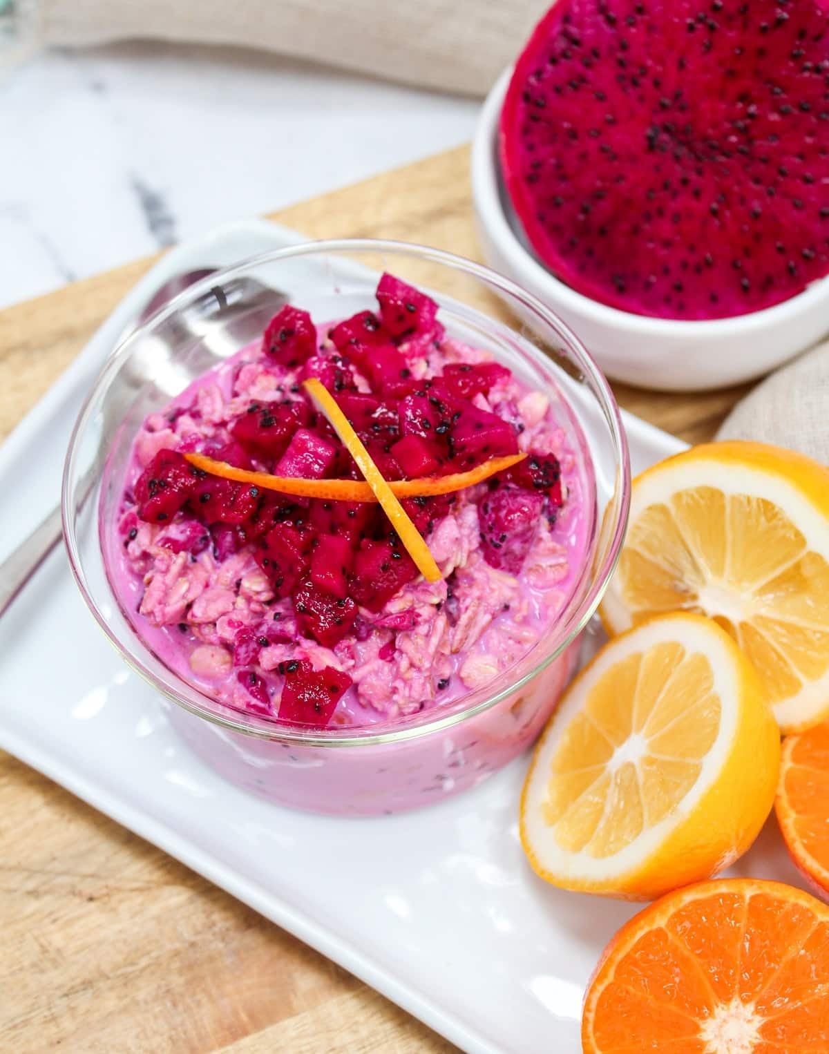 Pink overnight oats topped with chopped dragon fruit and citrus zest in a glass bowl.