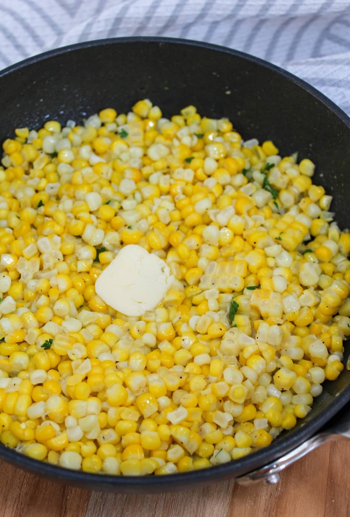Cooked corn in black skillet with butter on top.