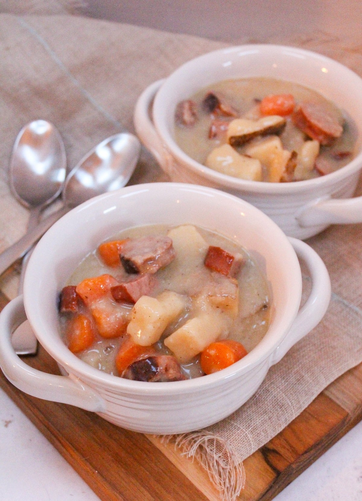 Chopped cooked carrots, onions, sausage, bratwurst, and potatoes in a creamy broth served in a white bowl.