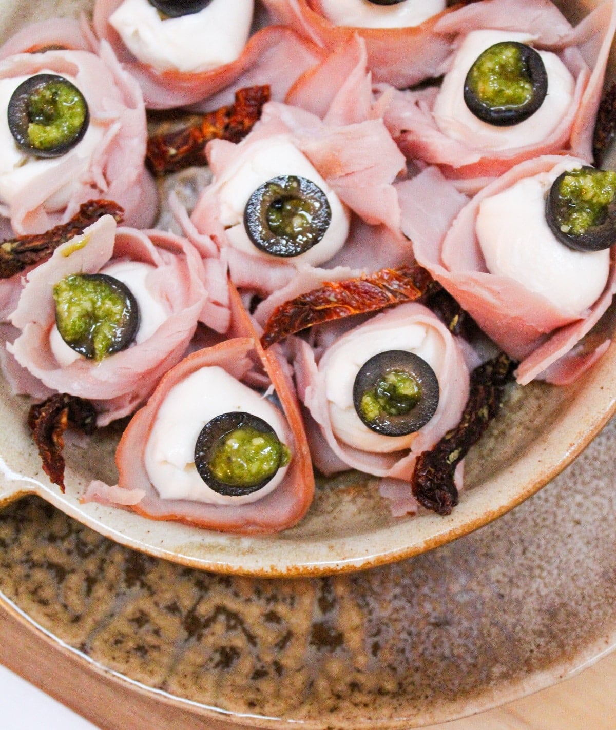 mozzarella balls wrapped in ham and topped with a black olive slice with pesto.
