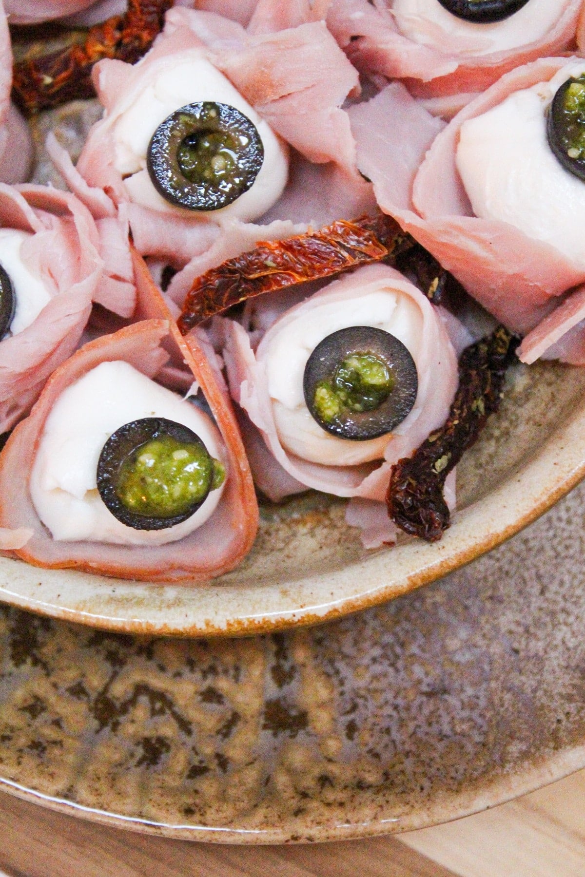 mozzarella balls wrapped in ham and topped with a black olive slice with pesto.