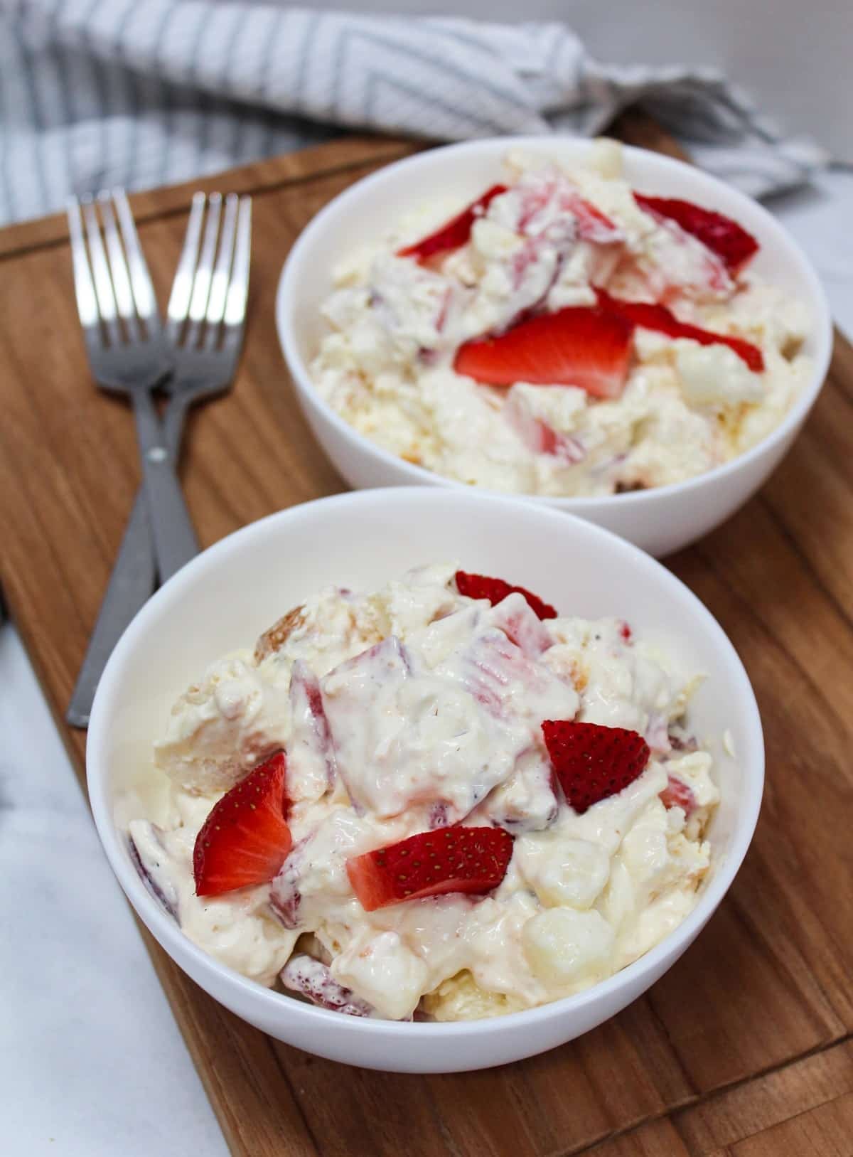 dessert conntaining strawberries, pudding, whipped topping, and angel food cake mixed together in a white bowl. 