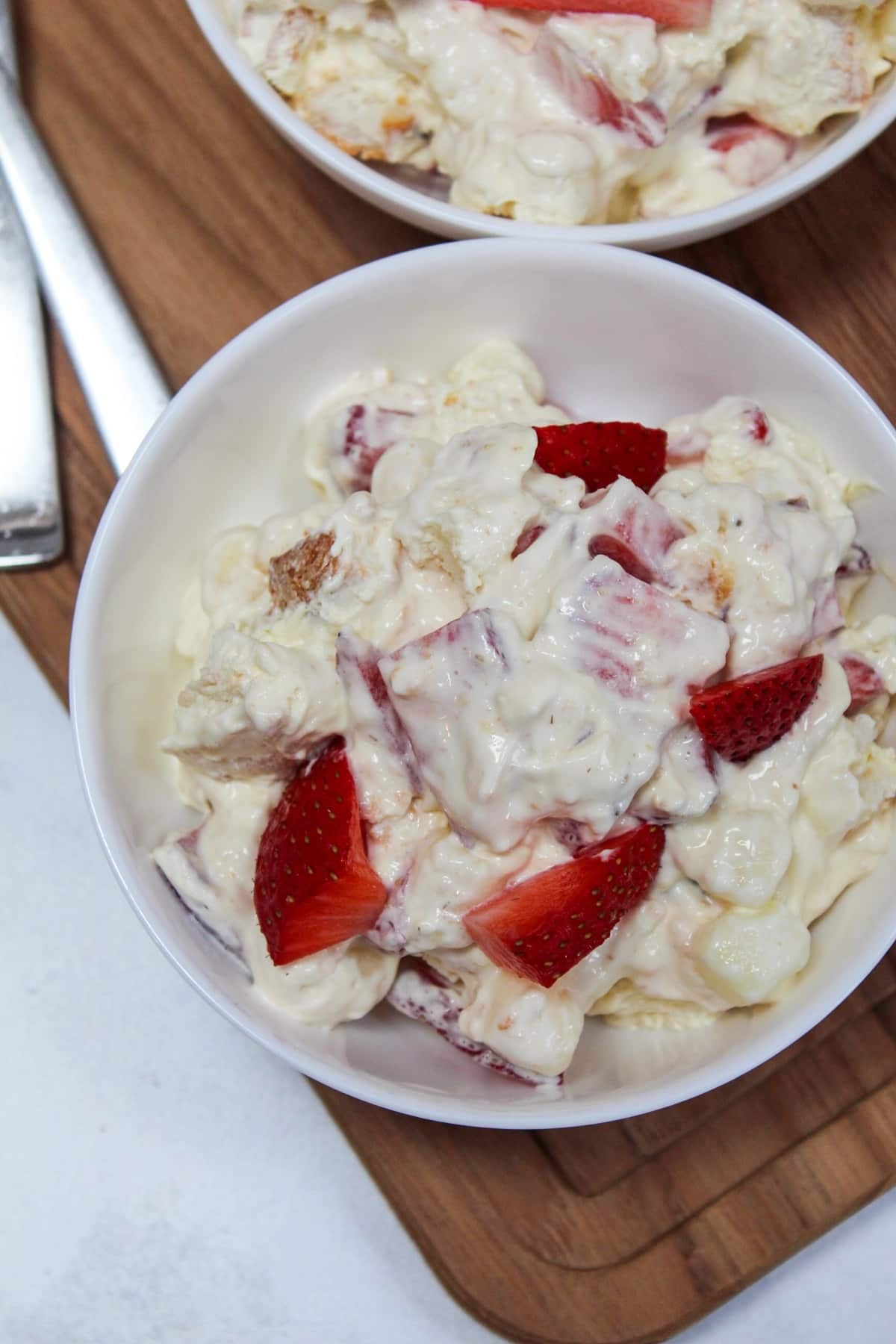 dessert conntaining strawberries, pudding, whipped topping, and angel food cake mixed together in a white bowl.