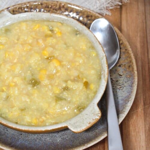 creamed corn with bits of chopped jalapenos in a brown bowl with a spoon on the side.