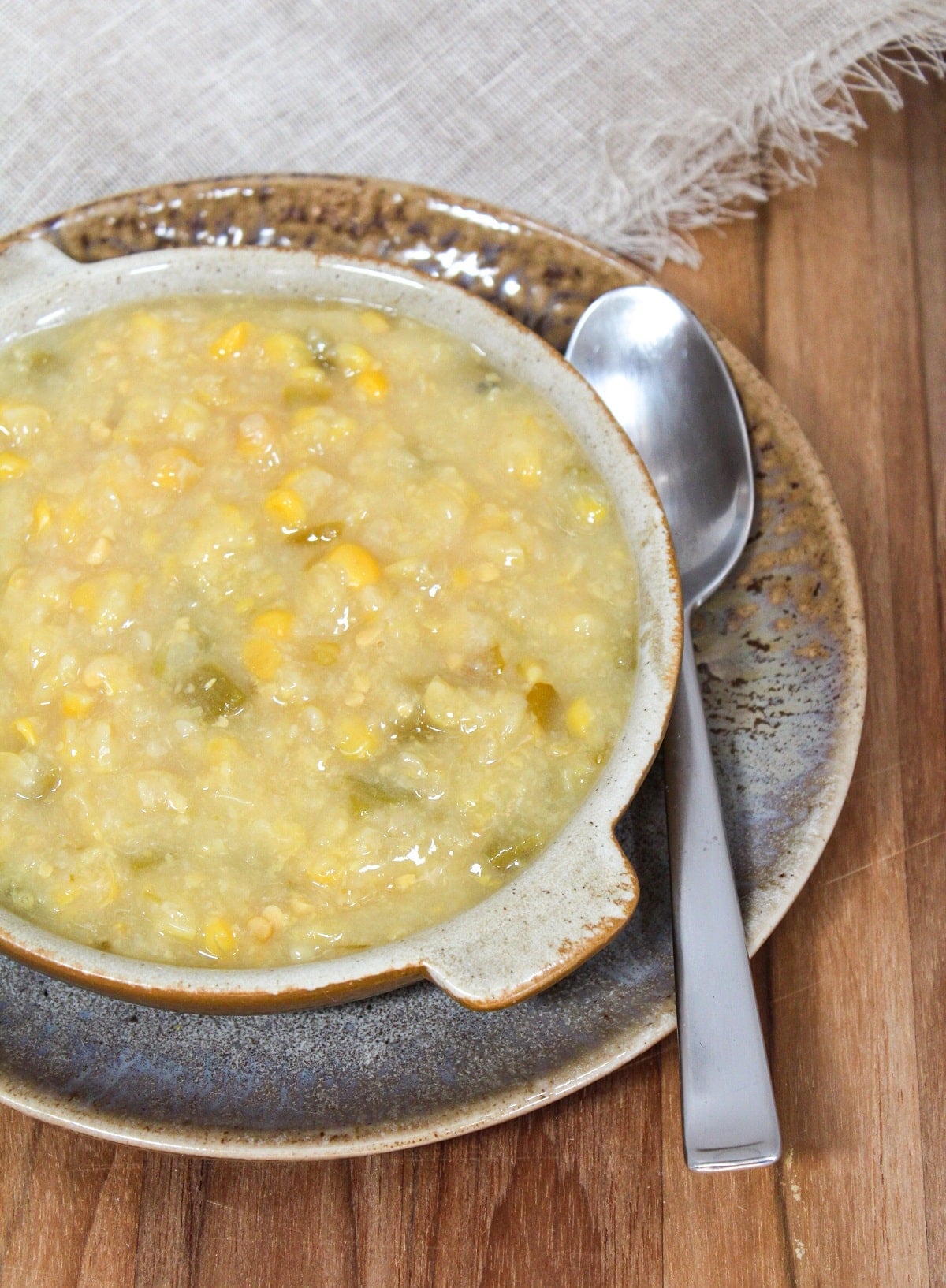 creamed corn with bits of chopped jalapenos in a brown bowl with a spoon on the side.