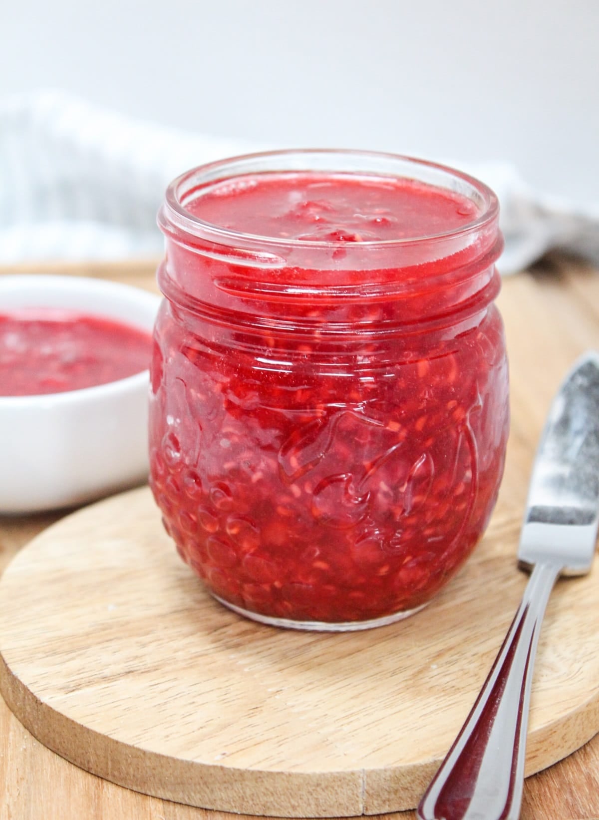 raspberry freezer jam in a glass jar with a knife on the side.
